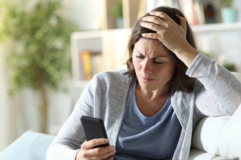 Une femme est assise sur un canapé et regarde son téléphone portable d'un air démoralisé.